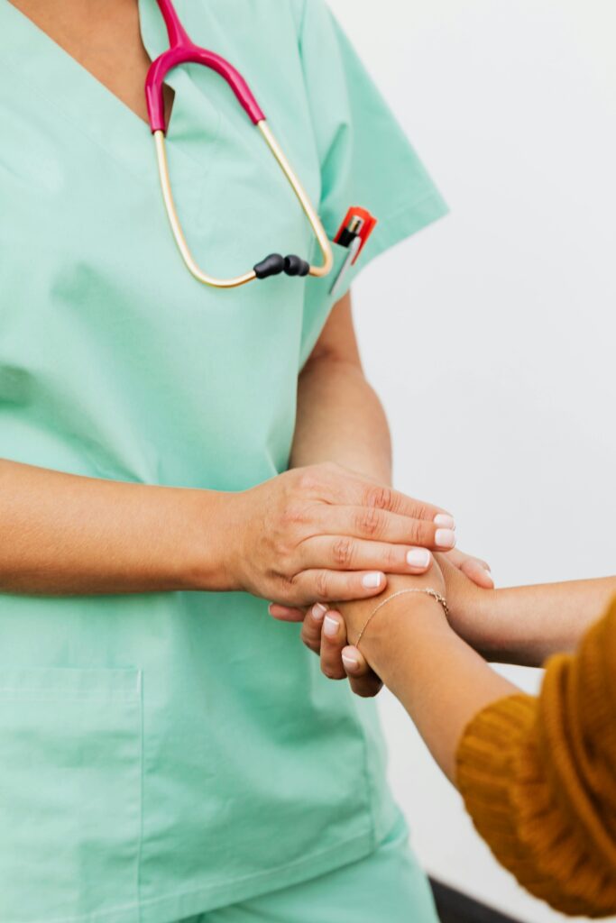 pexels-photo-5207015-5207015 A nurse in green scrubs gently clasps a patient's hand, offering support.